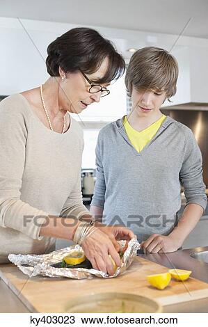 Stock Image - Elderly woman preparing seafood with her grandson in a kitchen. Fotosearch