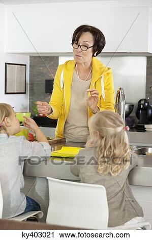 Stock Image - Elderly woman with her granddaughters in a kitchen. Fotosearch