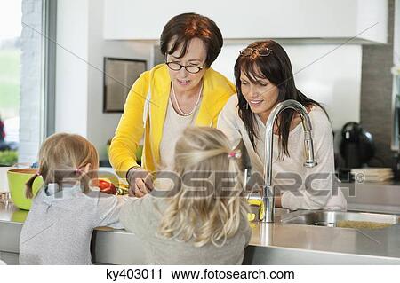 Stock Image - Two girls with her mother and grandmother working in a kitchen. Fotosearch
