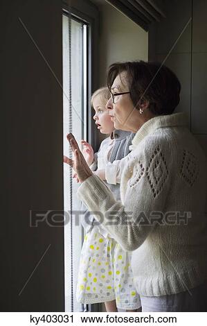 Stock Image - Woman with her granddaughter looking through a window. Fotosearch