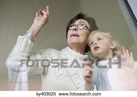 Woman with her granddaughter looking through a window View Large Photo Image Stock Photography - Woman with her granddaughter looking through a window. Fotosearch