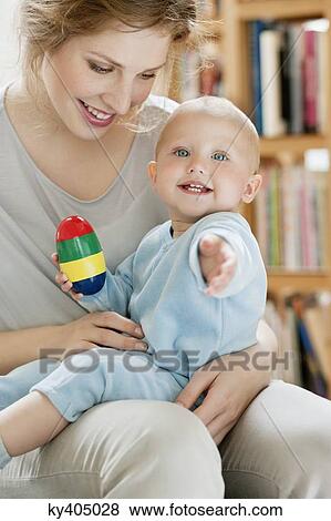 Baby girl sitting on the lap of her mother playing with a toy View Large Photo Image Stock Photo - Baby girl sitting on the lap of her mother playing with a toy. Fotosearch