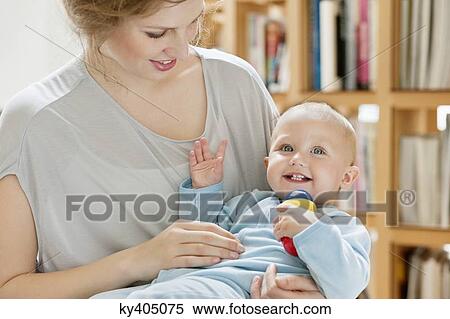 Baby girl sitting on the lap of her mother playing with a toy View Large Photo Image Stock Photography - Baby girl sitting on the lap of her mother playing with a toy. Fotosearch