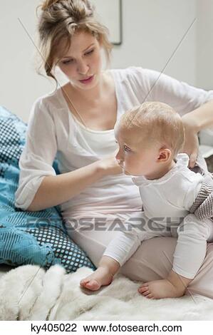 Stock Image - Woman putting on clothes to her daughter. Fotosearch