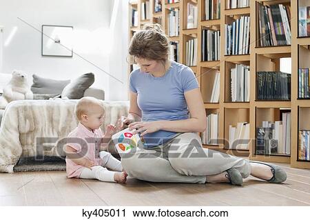 Stock Image - Woman sitting near her daughter playing with a toy. Fotosearch