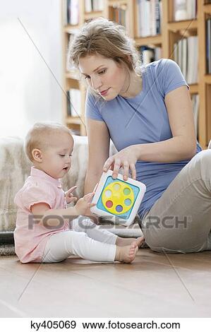 Stock Photo - Woman sitting near her daughter playing with a toy. Fotosearch