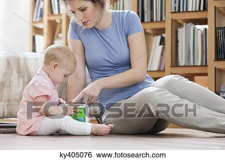 Stock Photograph - Woman sitting near her daughter playing with a toy. Fotosearch