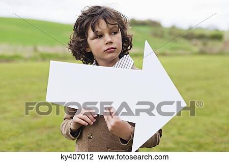 Stock Image - Boy holding an arrow sign in a field. Fotosearch