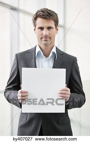 Businessman holding a blank placard in an office View Large Photo Image Stock Photo - Businessman holding a blank placard in an office. Fotosearch