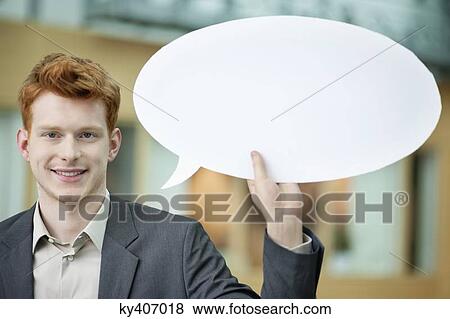 Businessman holding a speech bubble and smiling in an office View Large Photo Image Stock Photo - Businessman holding a speech bubble and smiling in an office. Fotosearch