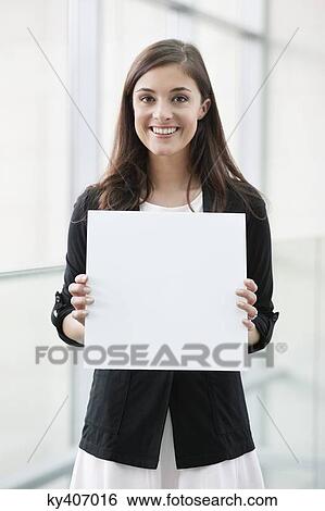 Portrait of a businesswoman holding a blank placard and smiling in an office View Large Photo Image Stock Photograph - Portrait of a businesswoman holding a blank placard and smiling in an office. Fotosearch