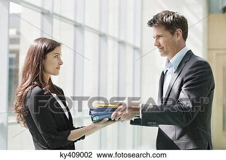 Businessmen giving files to his female colleague in an office View Large Photo Image Stock Image - Businessmen giving files to his female colleague in an office. Fotosearch