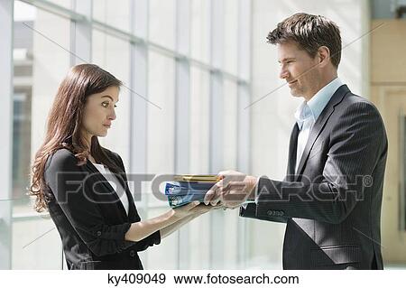 Stock Photo - Businessmen giving files to his female colleague in an office. Fotosearch