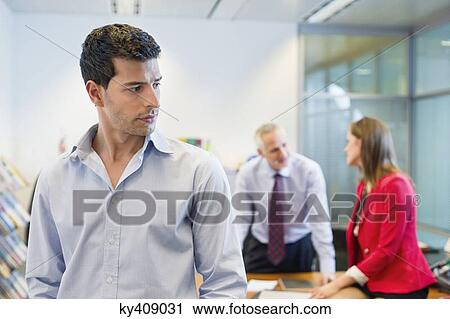 Stock Image - Male executive listening to his colleagues conversation in an office. Fotosearch