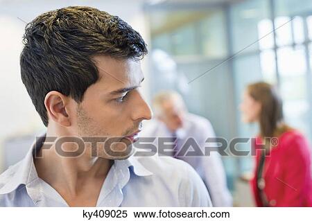 Stock Photography - Male executive listening to his colleagues conversation in an office. Fotosearch