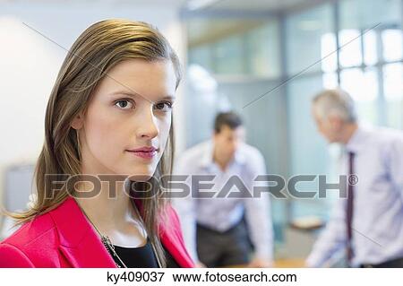 Stock Photo - Portrait of a businesswoman in an office with her colleagues discussing in the background. Fotosearch