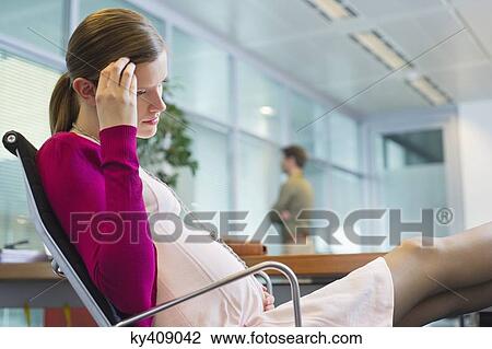 Stock Image - Pregnant woman sitting in the office. Fotosearch
