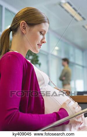 Stock Photography - Pregnant woman sitting in the office. Fotosearch
