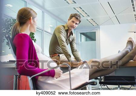 Stock Image - Pregnant woman talking to her colleague in the office. Fotosearch