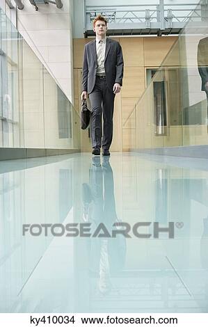 Businessman walking in an office corridor View Large Photo Image Picture - Businessman walking in an office corridor. Fotosearch
