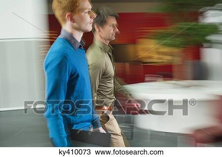Stock Image - Businessmen walking in an office corridor. Fotosearch