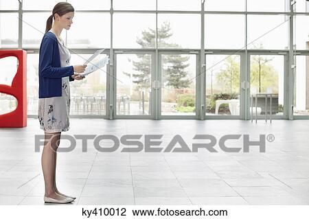Stock Image - Businesswoman holding documents and standing in an office lobby. Fotosearch