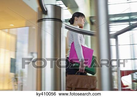 Stock Photograph - Businesswoman talking on a mobile and holding files and bag in an office. Fotosearch