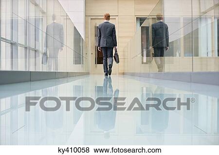 Rear view of a businessman walking in an office corridor View Large Photo Image Stock Photo - Rear view of a businessman walking in an office corridor. Fotosearch