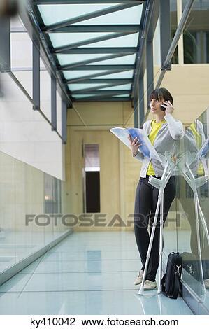 Woman holding a file and talking on a mobile phone in a corridor View Large Photo Image Stock Image - Woman holding a file and talking on a mobile phone in a corridor. Fotosearch