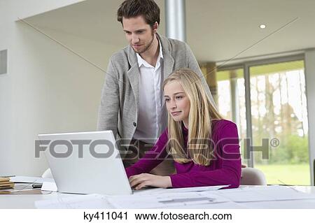 Man looking at a woman working on a laptop View Large Photo Image Stock Image - Man looking at a woman working on a laptop. Fotosearch