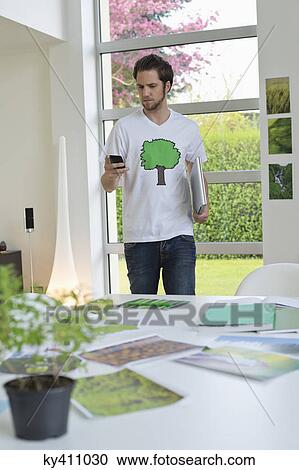 Stock Image - Man using a mobile phone with environment related posters in front of him on a table. Fotosearch
