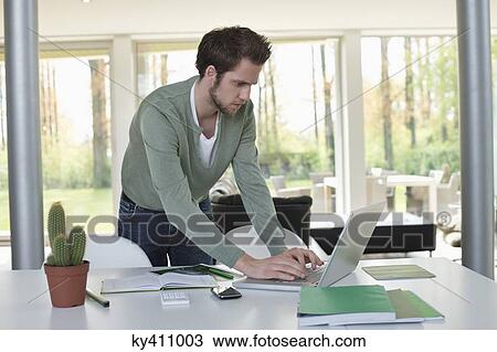 Stock Image - Man working on a laptop with a cactus plant on the table. Fotosearch