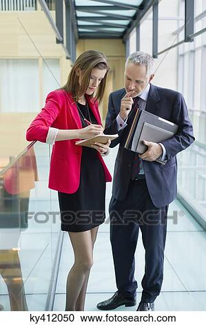 Stock Image - Business executives doing paperwork in an office corridor. Fotosearch