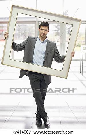Stock Photo - Businessman holding a frame in an office lobby. Fotosearch