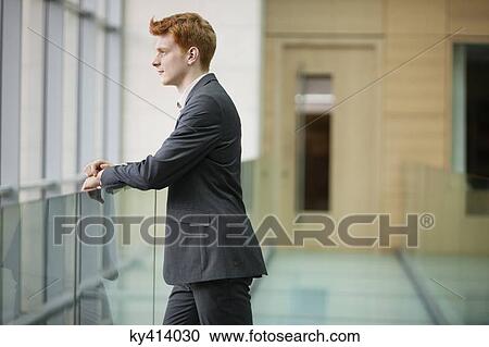 Stock Image - Businessman looking through glass window in a corridor. Fotosearch