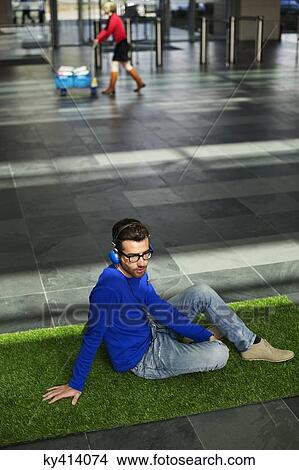 Businessman relaxing on grass and listening to music in an office lobby View Large Photo Image Picture - Businessman relaxing on grass and listening to music in an office lobby. Fotosearch