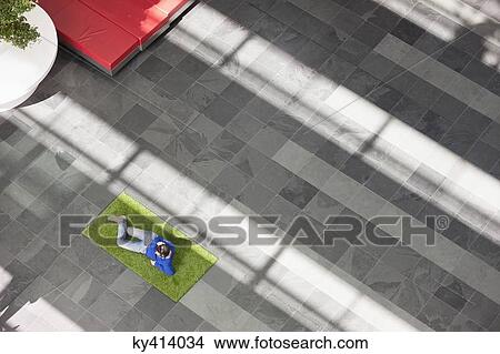 Picture - Businessman relaxing on grass in an office lobby. Fotosearch