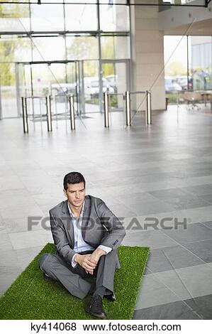 Stock Photo - Businessman relaxing on grass mat in an office lobby. Fotosearch