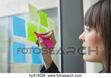 Stock Photo - Businesswoman drawing heart shape on an adhesive note in an office. Fotosearch