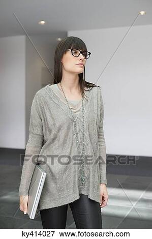 Stock Photo - Businesswoman holding a laptop and standing in an office. Fotosearch