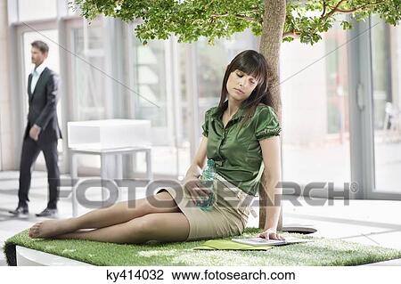 Stock Image - Businesswoman relaxing on grass mat. Fotosearch