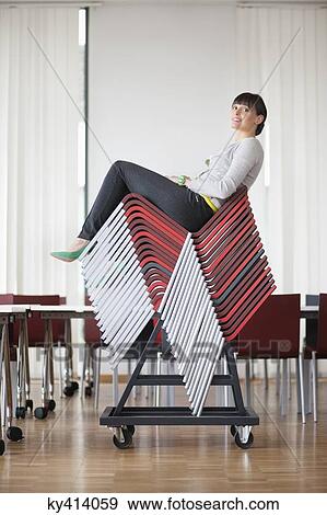 Stock Photo - Businesswoman sitting on pileup chairs in an office. Fotosearch