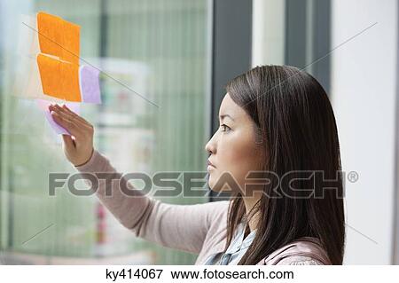 Picture - Businesswoman sticking memo notes on glass in an office. Fotosearch - Search Stock Photography, Photos, Prints, Images, and Photo Clipart
