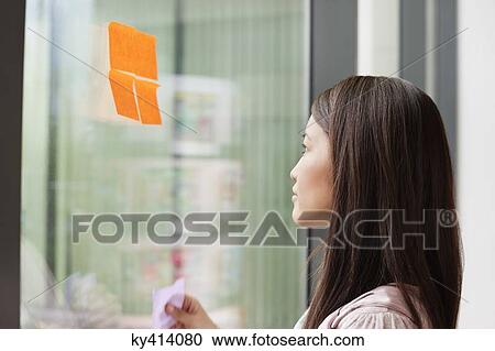 Stock Image - Businesswoman sticking memo notes on glass in an office. Fotosearch