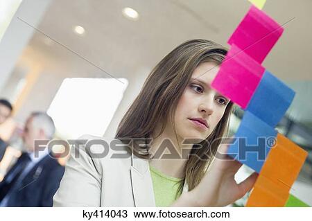 Businesswoman sticking memo notes on glass in an office View Large Photo Image Stock Photo - Businesswoman sticking memo notes on glass in an office. Fotosearch - Search Stock Images, Poster Photographs, Pictures, and Clip Art Photos
