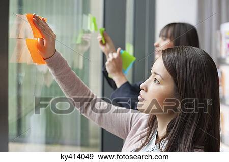 Businesswomen sticking memo notes on glass in an office View Large Photo Image Stock Photo - Businesswomen sticking memo notes on glass in an office. Fotosearch