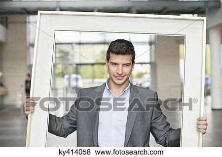 Stock Photo - Close-up of a businessman holding a frame in an office lobby. Fotosearch