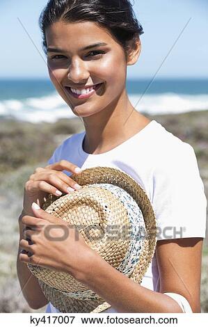 Stock Photo - Beautiful woman holding a hat on the beach. Fotosearch