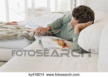 Man lying on the bed and reading a magazine View Large Photo Image Picture - Man lying on the bed and reading a magazine. Fotosearch