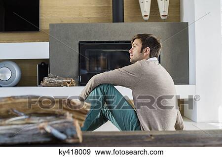 Man sitting in front of a fireplace at home View Large Photo Image Stock Photo - Man sitting in front of a fireplace at home. Fotosearch